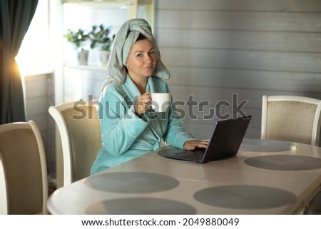 woman after shower, in the morning, with a cup of coffee working with a laptop