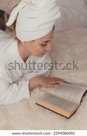 a woman after a shower with a turban on her head lies on the bed reading a book