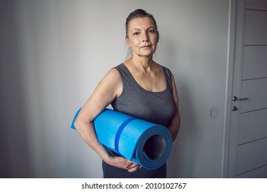 woman aged athlete stands in a white room with a yoga mat