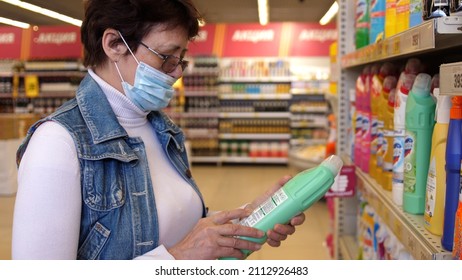 Woman In Aged Wearing Face Mask And Eye Glasses During Coronavirus Shopping And Stocking Up For Household Chemicals At Supermarket.