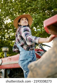 Woman Agriculture Worker Or Farmer On Tractor Working Farm During Harvest Time. Sustainability Farming In The Countryside. Serious Girl Farming In A Field, Fresh Produce For Farmers Market