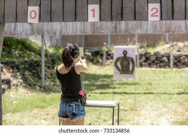 Woman aiming pistol at target out indoor firing range or shooting range.