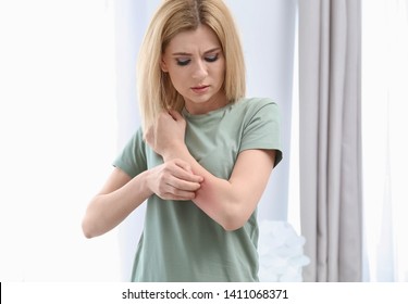 Woman with allergy symptoms scratching forearm indoors