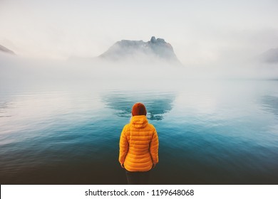 Woman alone looking at foggy sea traveling adventure lifestyle outdoor solitude sad emotions winter down jacket clothing cold scandinavian minimal landscape
