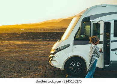 Woman alone traveler enjoy outdoor leisure activity traveling with a big modern camper motor home van rv. Beautiful sunset in background. Freedom and independence with alternative lifestyle people