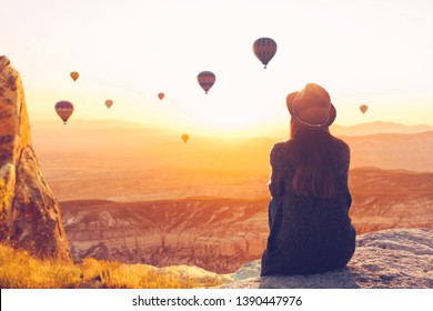A woman alone unplugged sits on top of a mountain and admires the flight of hot air balloons in Cappadocia in Turkey. Digital detox and soul search