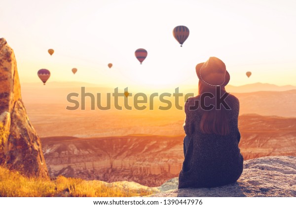 A woman alone unplugged sits on top of a\
mountain and admires the flight of hot air balloons in Cappadocia\
in Turkey. Digital detox and soul\
search