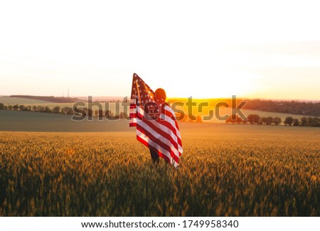 Woman with the American flag in a wheat field at sunset. 4th of July.  Independence Day, Patriotic holiday.