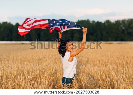 Woman with American flag in wheat field at sunset. 4th of July. Independence Day patriotic holiday