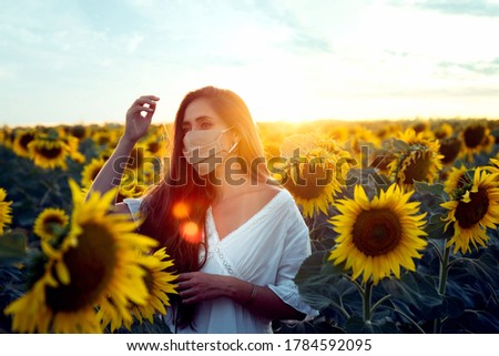 Woman among sunflowers with face mask putting on hair at sunset