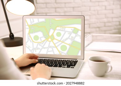 Woman analyzing cadastral map on laptop at table, closeup 