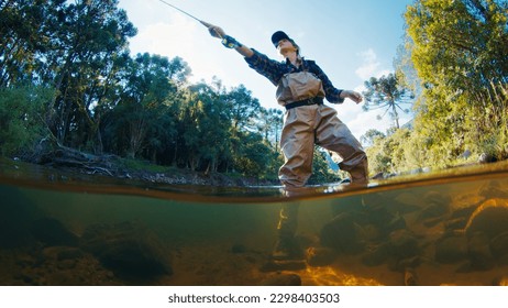 Woman angler on the river. Woman stands in the water in waders and casts the line. Woman fishing on the river - Powered by Shutterstock