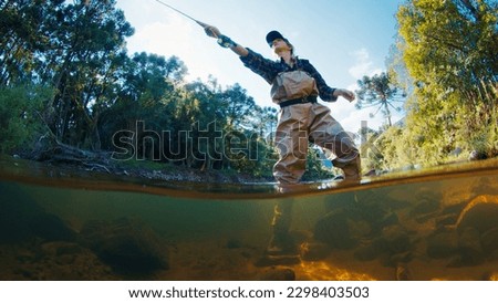 Woman angler on the river. Woman stands in the water in waders and casts the line. Woman fishing on the river
