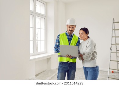 Woman apartment owner discussing home design plan with foreman. Professional builder showing project of renovation to young woman using laptop computer. Building and home renovation - Powered by Shutterstock