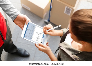 Woman appending signature after receiving parcel from courier outdoors