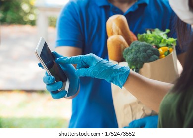 Woman Appending Signature In Digital Mobile Phone After Grocery Store Delivery Man Wearing Blue Shirt Delivering Food To A Woman At Home.delivery Service During Covid19.New Normal.