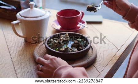 A woman with appetite and pleasure eats a traditional Caucasian lamb dish with herbs and herbs, sitting in a national restaurant near the window.