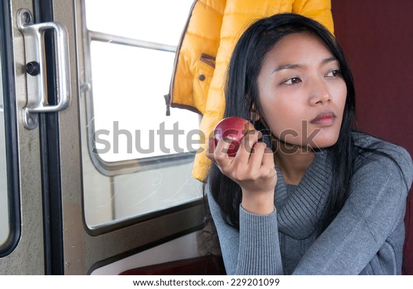 Woman with an apple sitting on a\
train. Healthy snacks of fruit in a train on a trip. Passengers\
girl eat red apple when traveling by public\
transport..
