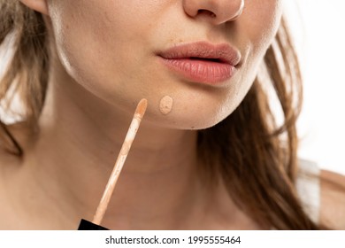 A Woman Applies Concealer To A Pimple On Her Chin On A White Background