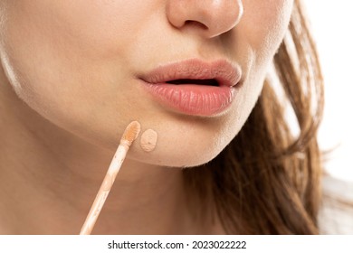 A Woman Applies Concealer To A Pimple On Her Chin On A White Background