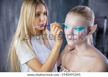 Woman applies creative makeup to the face of a young model