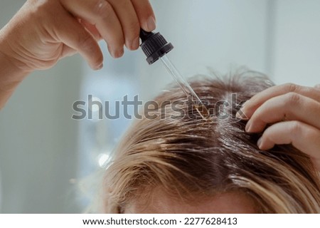  Woman applies oil to her hair with pipette. Beauty caring for scalp and hair. 