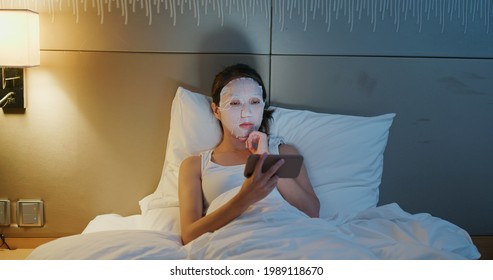 Woman apply face mask and use of mobile phone on bed at night - Powered by Shutterstock