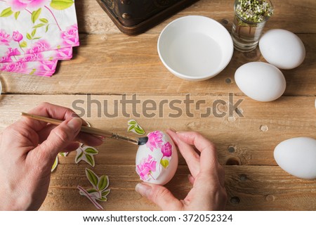 woman apply  glue on colored Easter egg, with the technique of decoupage