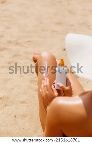 Woman apply sun protection cream on her smooth tanned legs.