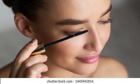 Woman Applying Black Mascara On Eyelashes With Makeup Brush, Grey Background