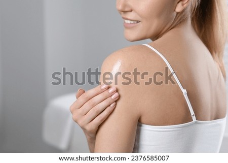 Woman applying body oil onto shoulder indoors, closeup. Space for text