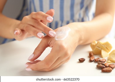 Woman applying cocoa butter lotion onto hand over table