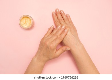 Woman applying cosmetic cream on her hands. Female elderly hands. Skincare. Senior woman. Pink background.  - Shutterstock ID 1969756216
