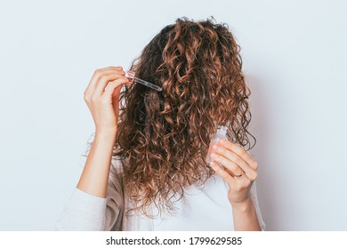 Woman Applying Cosmetic Oil To Her Beautiful Curly Hair, Close-up On White Background