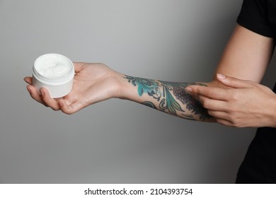 Mujer aplicando crema en el brazo con tatuajes sobre fondo gris claro, cerrado