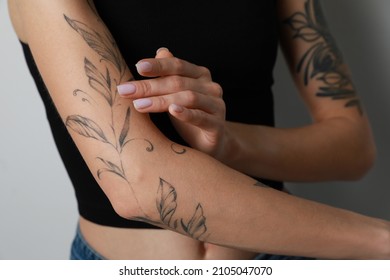 Woman applying cream on her arm with tattoos against light background, closeup - Shutterstock ID 2105047070