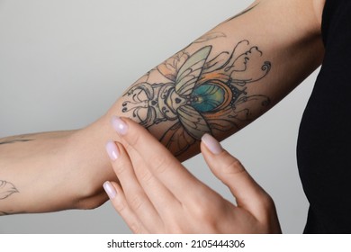 Woman applying cream on her arm with tattoos against light background, closeup