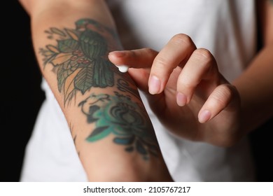 Woman applying cream on her arm with tattoos against black background, closeup - Shutterstock ID 2105767217