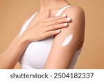 Woman applying cream onto arm on beige background, closeup. Body care