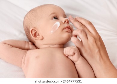 Woman applying cream onto baby`s face on bed, closeup - Powered by Shutterstock