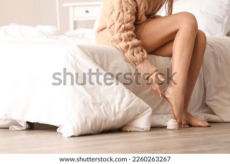Woman applying cream onto her feet in bedroom