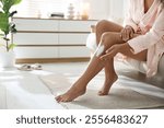 Woman applying cream onto leg on sofa at home, closeup. Space for text