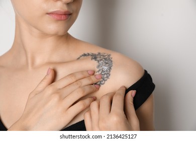 Mujer aplicando crema en el tatuaje sobre su piel contra fondo claro, cerrar