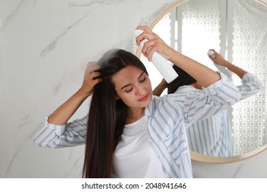 Woman applying dry shampoo onto her hair near mirror - Shutterstock ID 2048941646