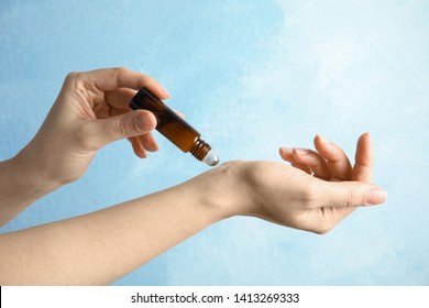 Woman Applying Essential Oil On Her Wrist Against Color Background, Closeup