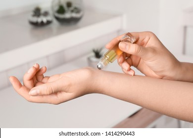 Woman applying essential oil on wrist indoors, closeup
