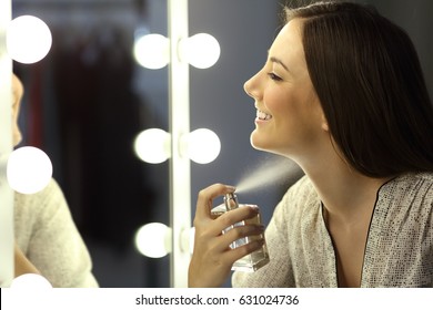 Woman applying fragrance with a spray in front of a make up mirror