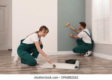 Woman applying glue onto wall paper while man hanging sheet indoors - Shutterstock ID 1996882262