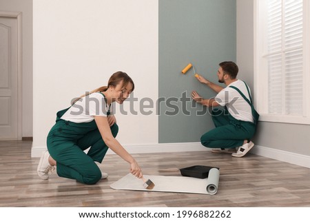Woman applying glue onto wall paper while man hanging sheet indoors