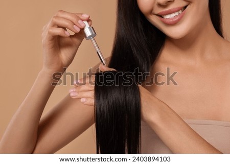 Woman applying hair serum on beige background, closeup. Cosmetic product